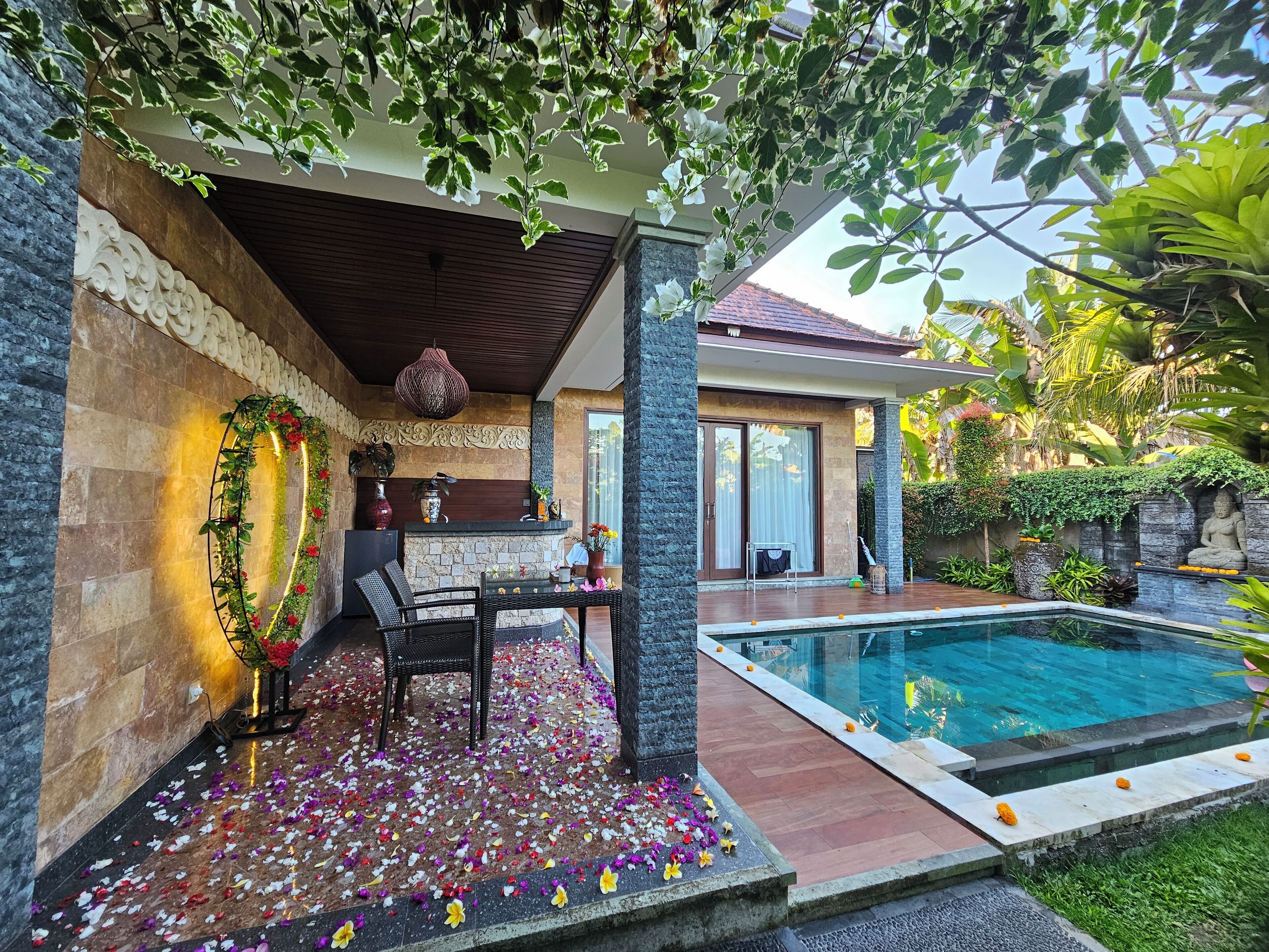 A poolside area with a stone bench, a table with chairs, and a decorative wall with a hanging light fixture.