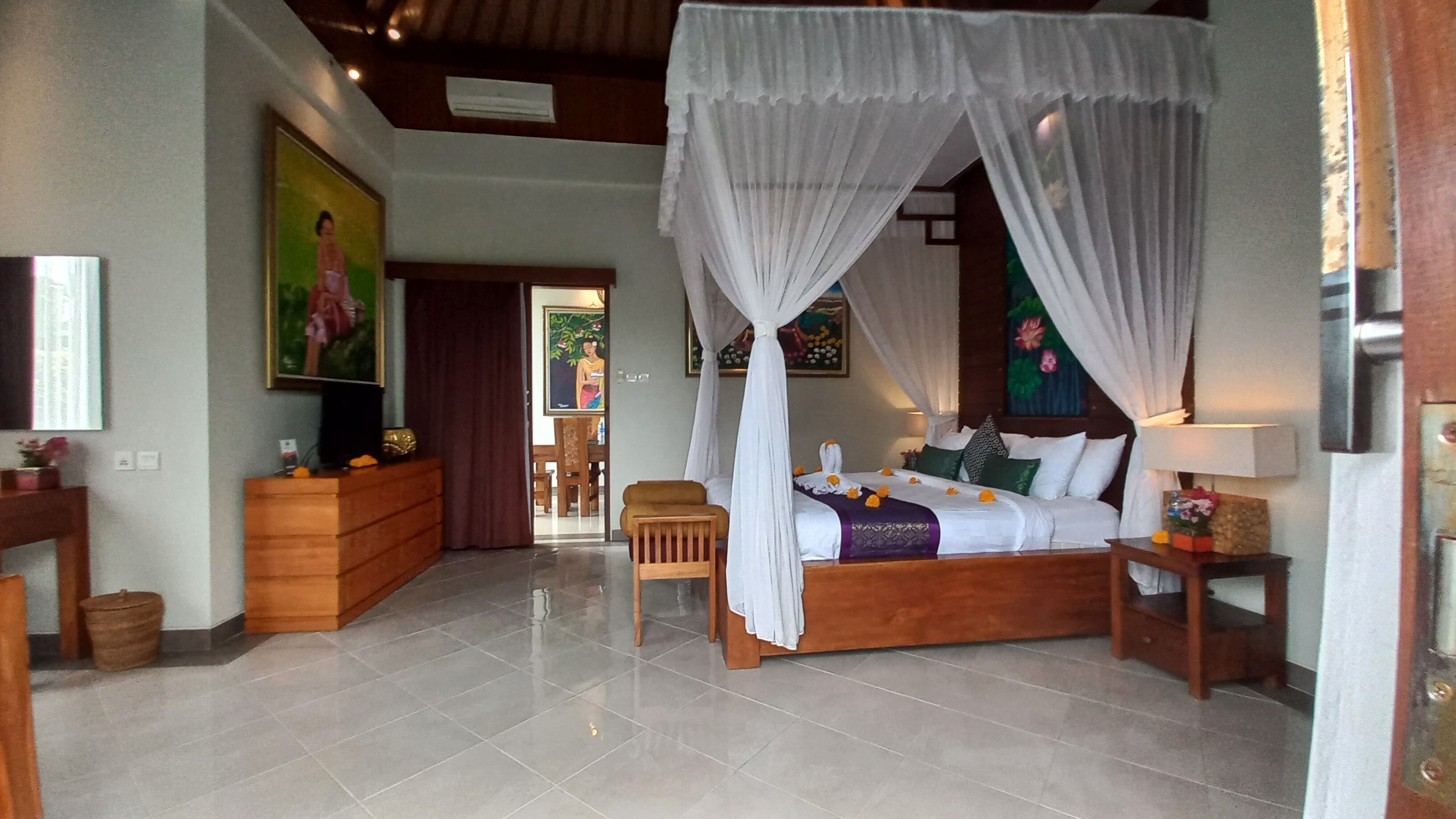 A bedroom with a four-poster canopy bed, wooden furniture, and artwork on the walls.