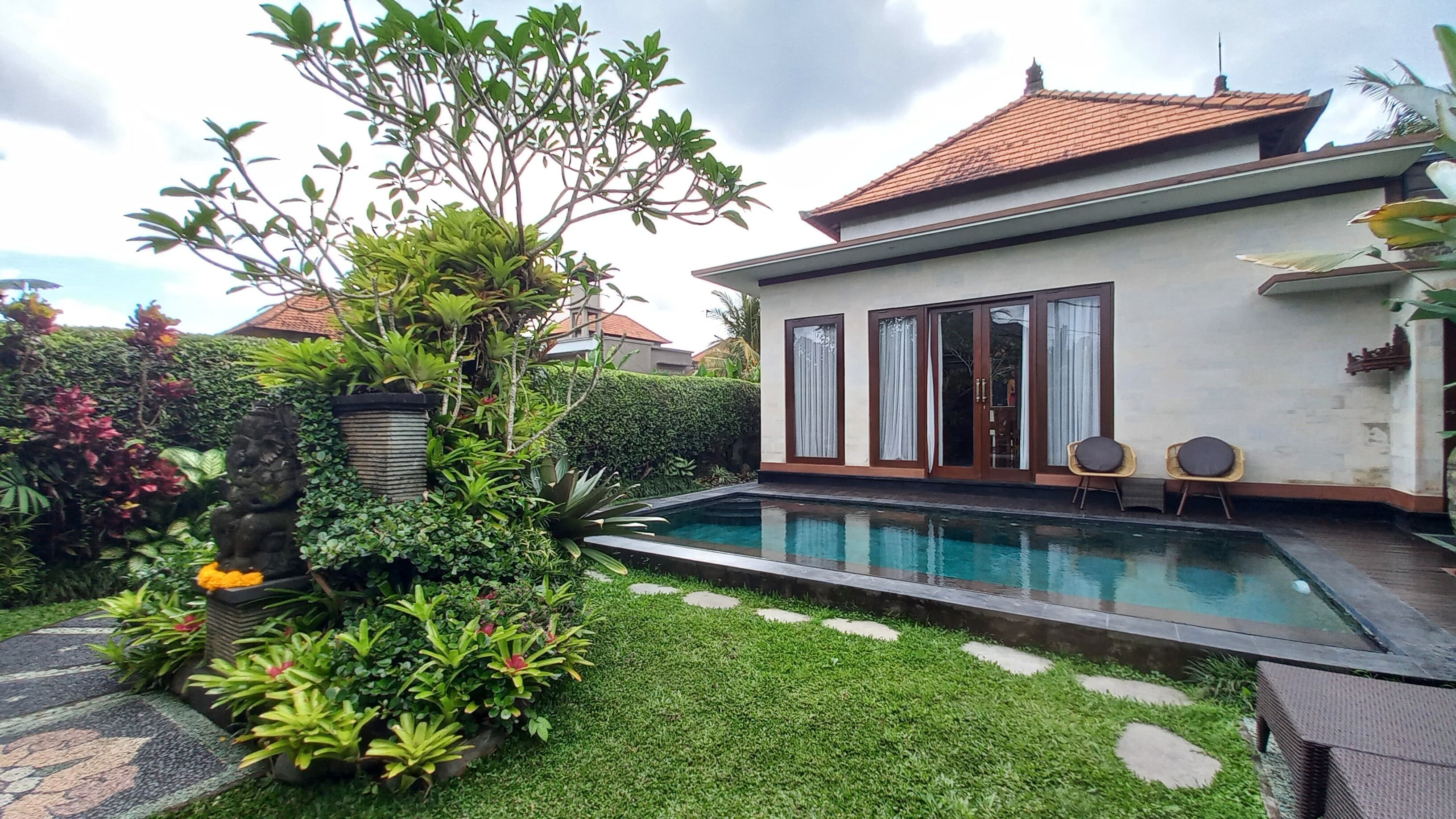 Ein modernes Haus mit Swimmingpool, umgeben von üppiger Vegetation und einer Steinstatue.