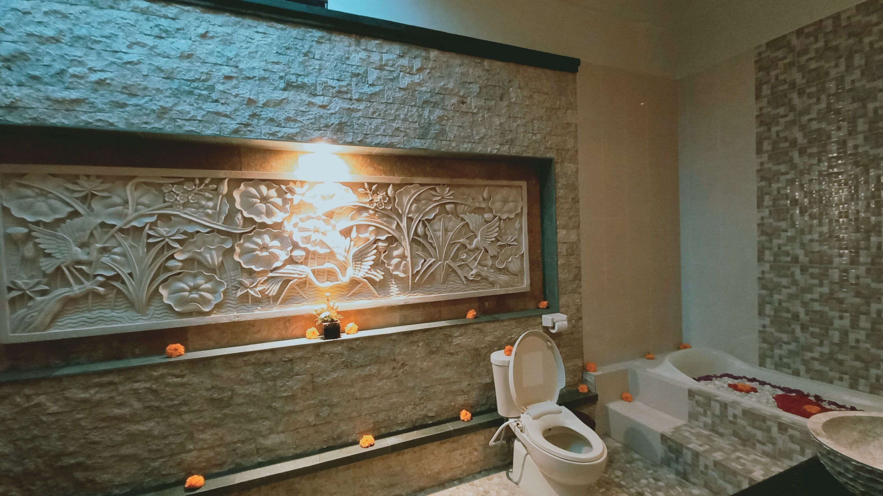 Une salle de bain avec un mur en pierre, un panneau décoratif, des toilettes et une baignoire.