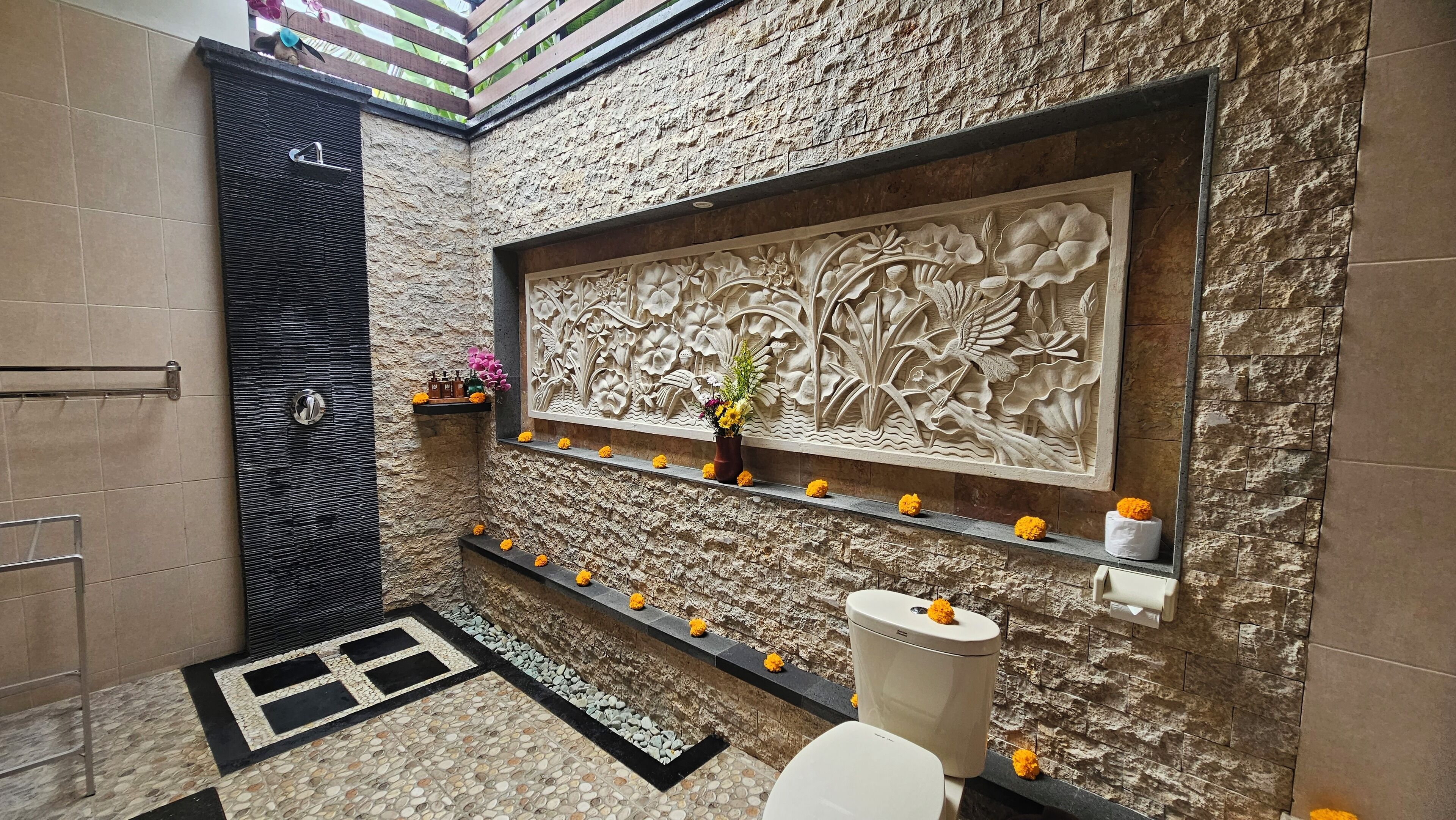 Een badkamer met een stenen muur, een houten plank met bloemen, een decoratief paneel en een toilet.
