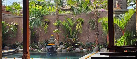 A covered outdoor area with a pool, surrounded by tropical plants and a stone wall.