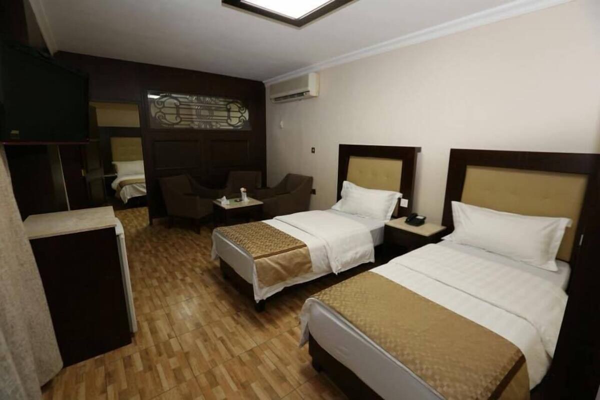 A hotel room with two beds, a desk, a chair, and a small seating area.