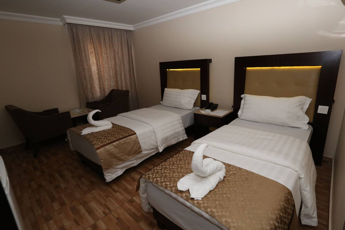 A hotel room with two beds, a wooden floor, a desk, and a chair.