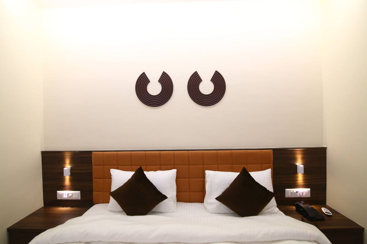 Camera d'albergo con un letto, due lampade ai comodini, una luce a parete e due elementi decorativi.