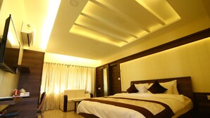 A modern hotel room with a large bed, a desk, and a seating area. - GD Hotel (Navsari)