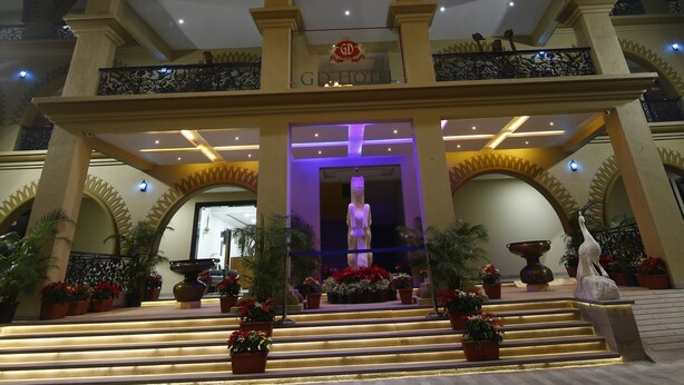 A grand lobby with a chandelier, multiple staircases, and a statue. - GD Hotel (Navsari)