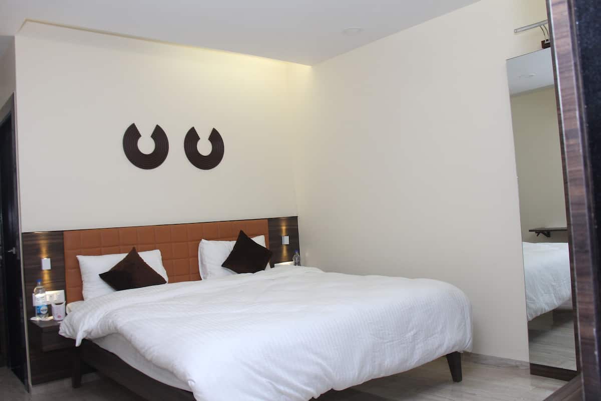 Camera d'albergo con un letto grande, una testiera in legno, due luci a parete e uno specchio.