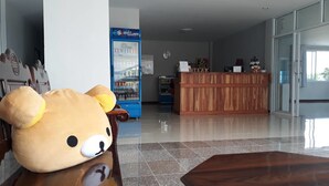 A reception area with a wooden desk, a plush bear, a blue vending machine, and a reception desk with a sign. - Golden Teak Ville (Buriram)