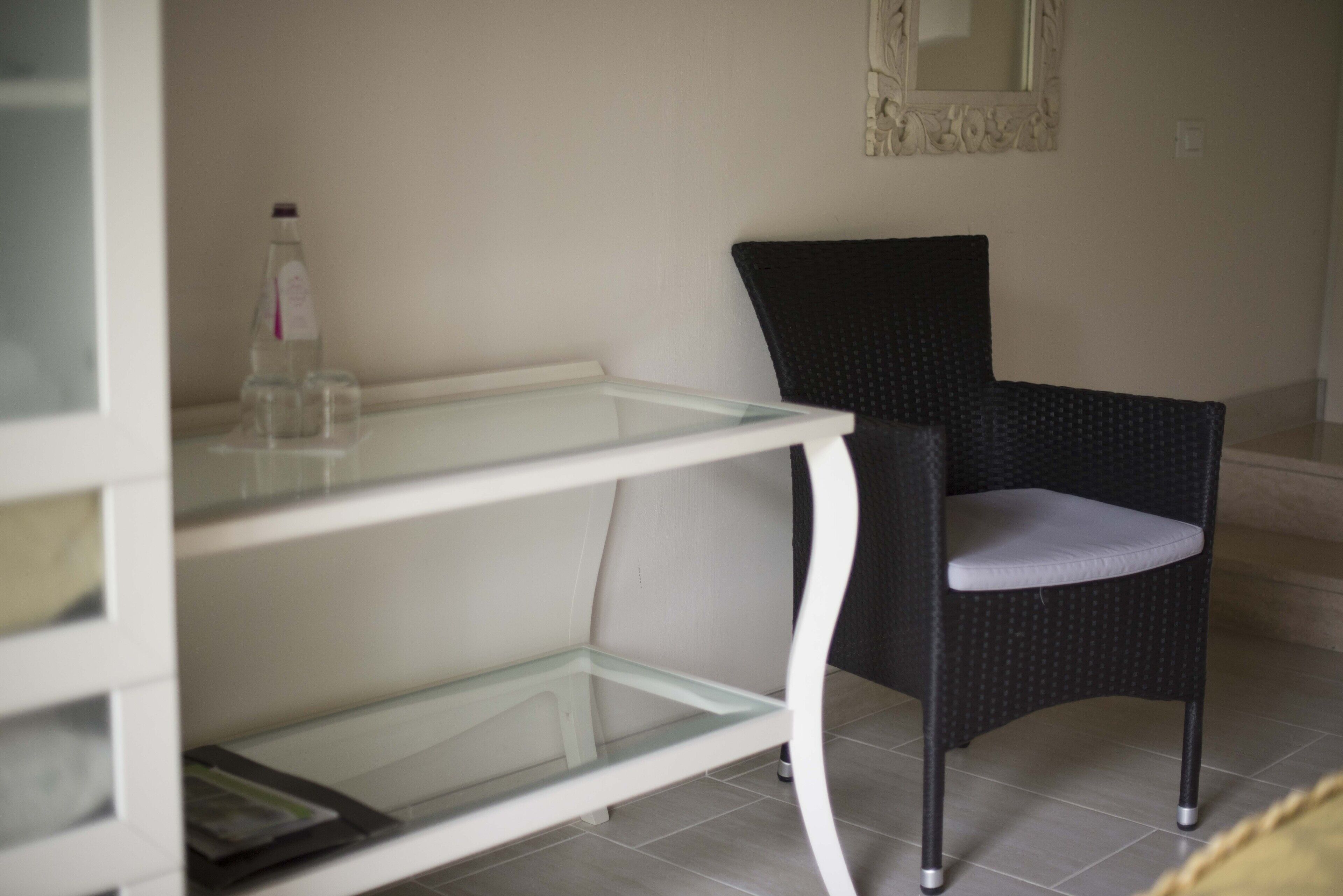 A room with a glass-top table, a black chair with a cushion, and a mirror on the wall.