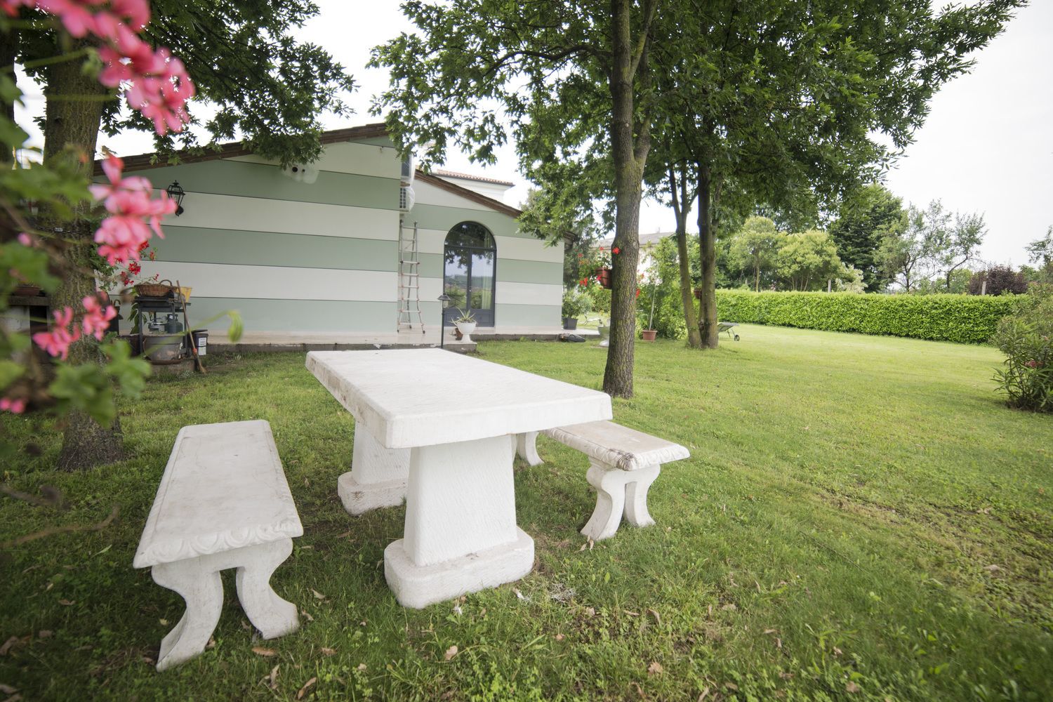 Un espace extérieur aménagé avec des sièges blancs, comprenant une table et des bancs, entouré d’une pelouse bien entretenue et d’arbres.