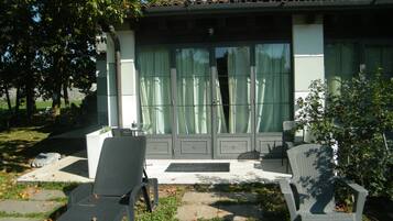 Ein Terrassenbereich mit zwei Liegestühlen und einem kleinen Tisch, ein Ziegeldach und ein Gebäude mit großen Fenstern und Vorhängen.