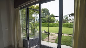 A room with a large sliding glass door leading to a well-maintained garden with a lawn, hedges, and a pathway. - Villa Franca in Franciacorta (Passirano)