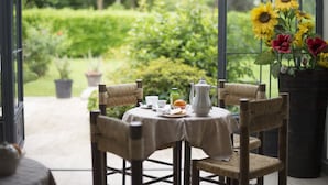 A conservatory with a table set for breakfast, surrounded by wicker chairs, with a view of a garden and potted plants. - Villa Franca in Franciacorta (Passirano)