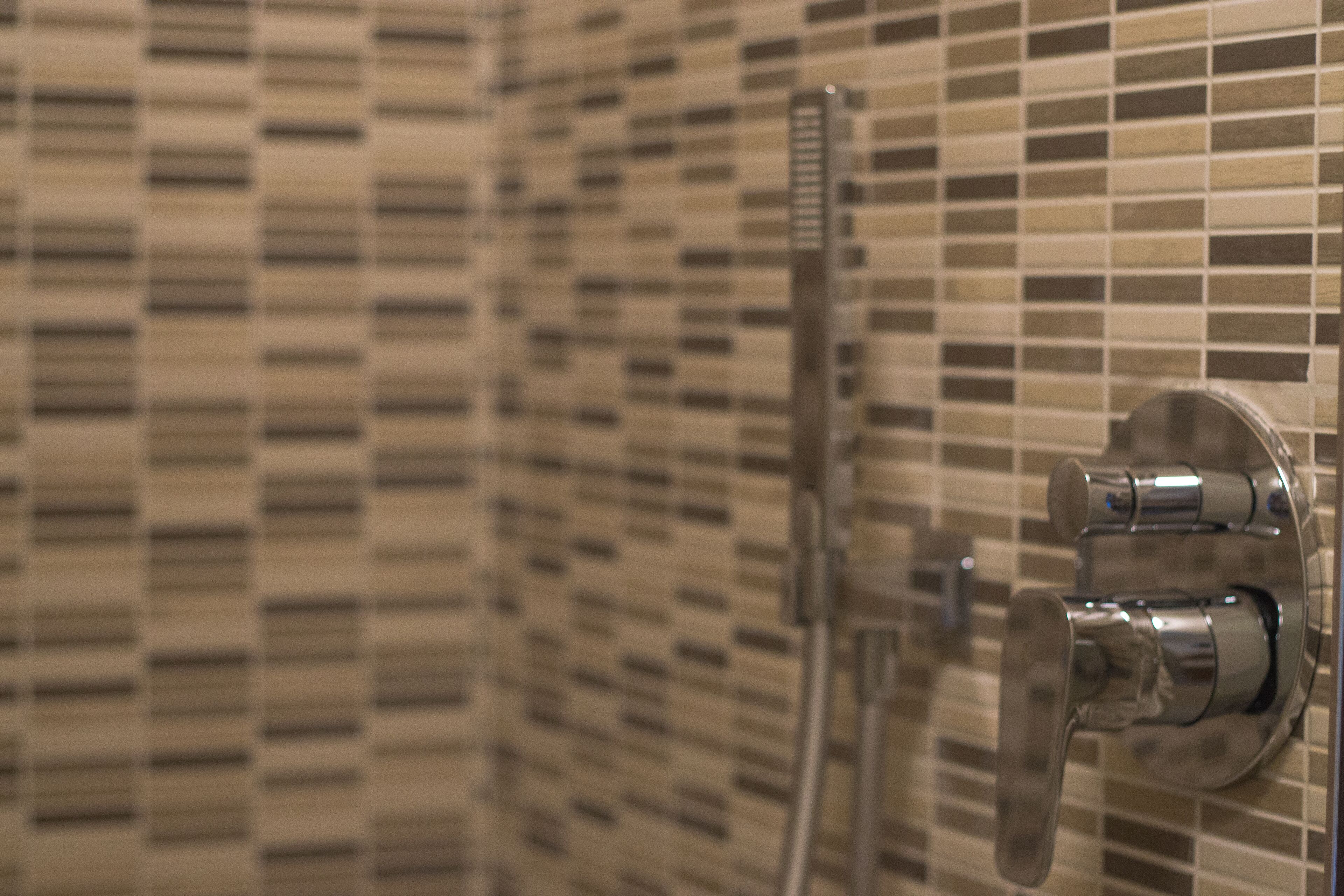 A bathroom with a tiled wall and a chrome showerhead.
