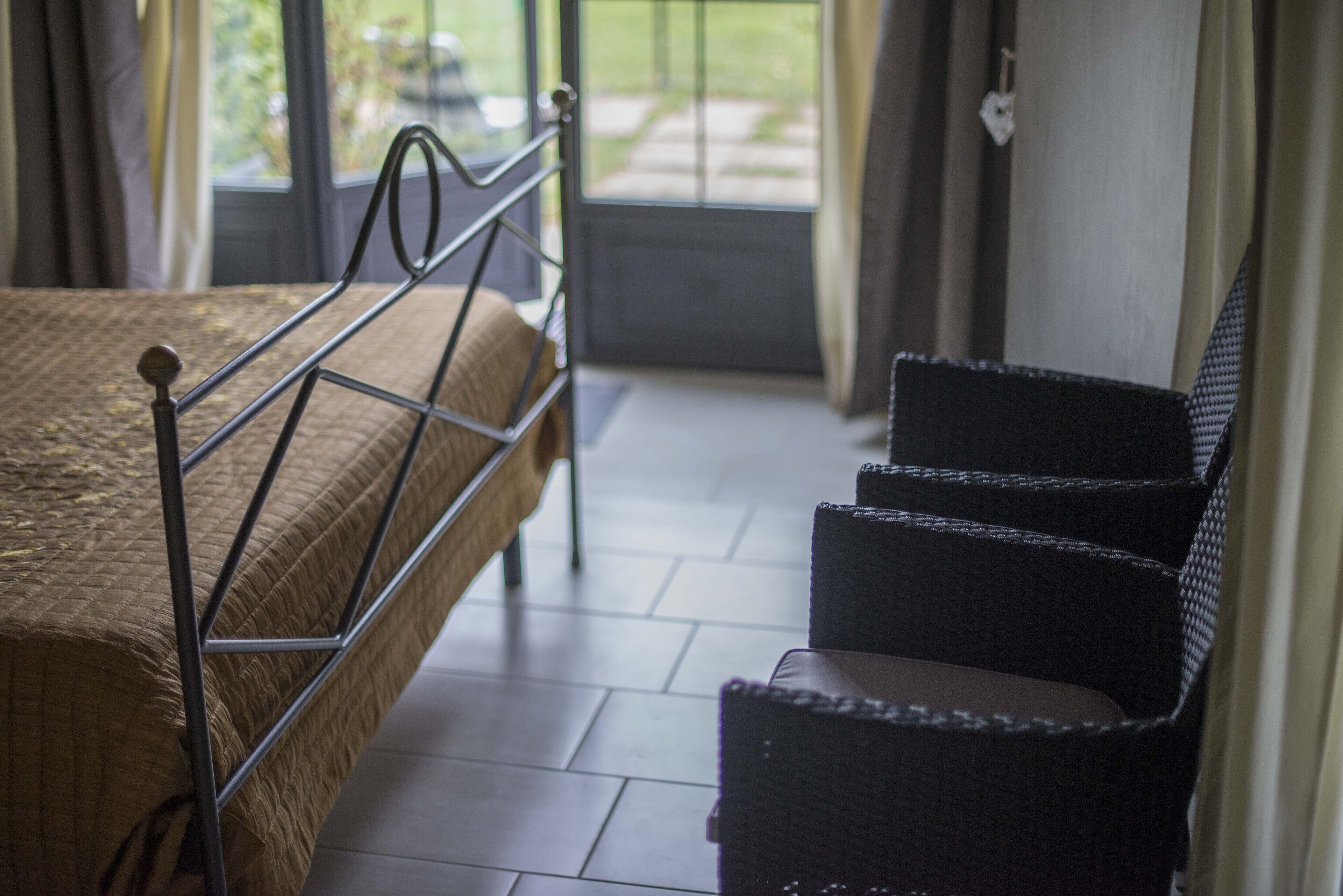 Een slaapkamer met een bed, een stoel en uitzicht op de omgeving via een deur.