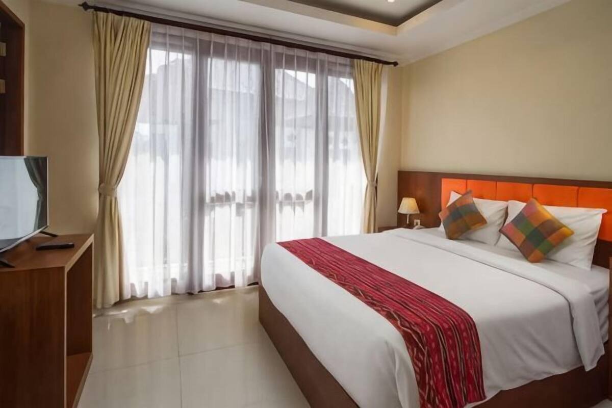 A hotel room with a large bed, curtains, a TV, and a nightstand.