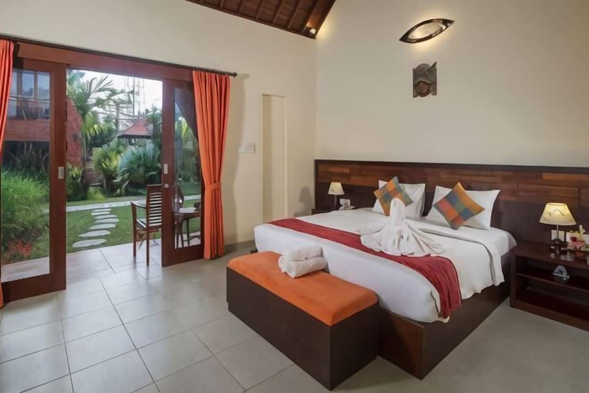 A bedroom with a bed, a nightstand, a bench, a door, and a view of the garden.
