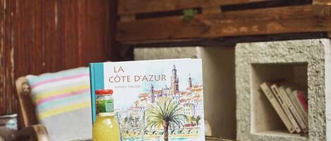 A book titled "La Côte d'Azur" by Andrea Terlizzi on a round table with a glass of yellow drink and a decorative plate.