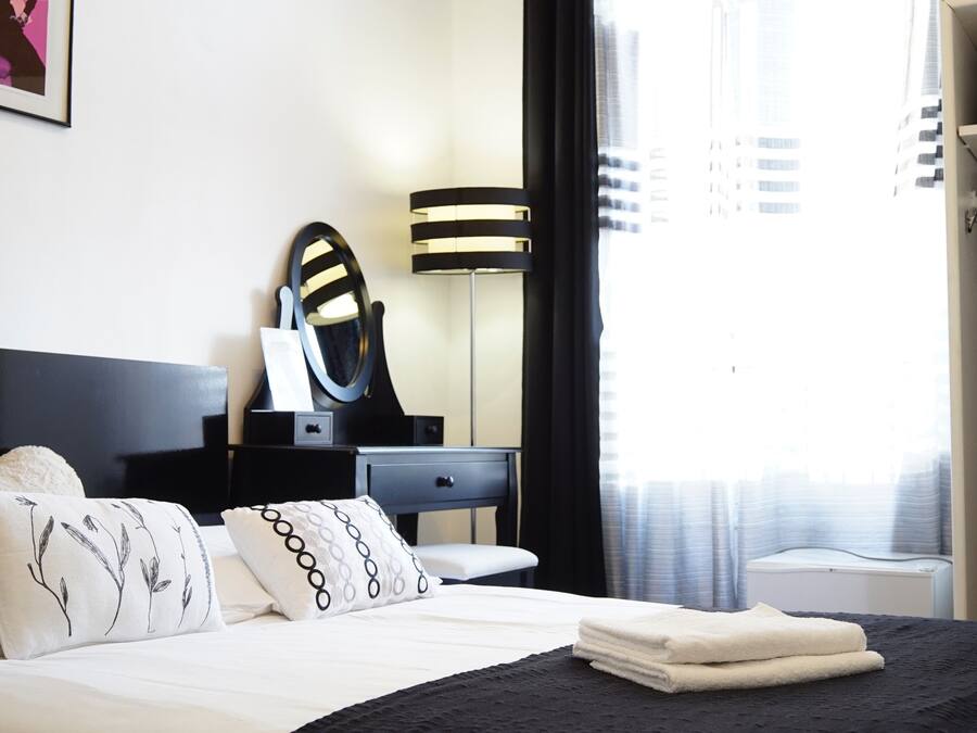 Una habitación de hotel con una cama, una mesita de noche con lámpara, un espejo y un armario.
