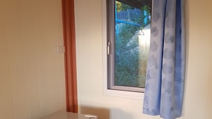 Una habitación pequeña con un refrigerador blanco, una ventana con cortina azul y piso de madera.