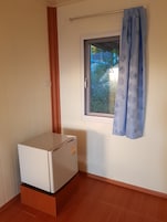 Una habitación pequeña con un refrigerador blanco, una ventana con cortina azul y piso de madera.