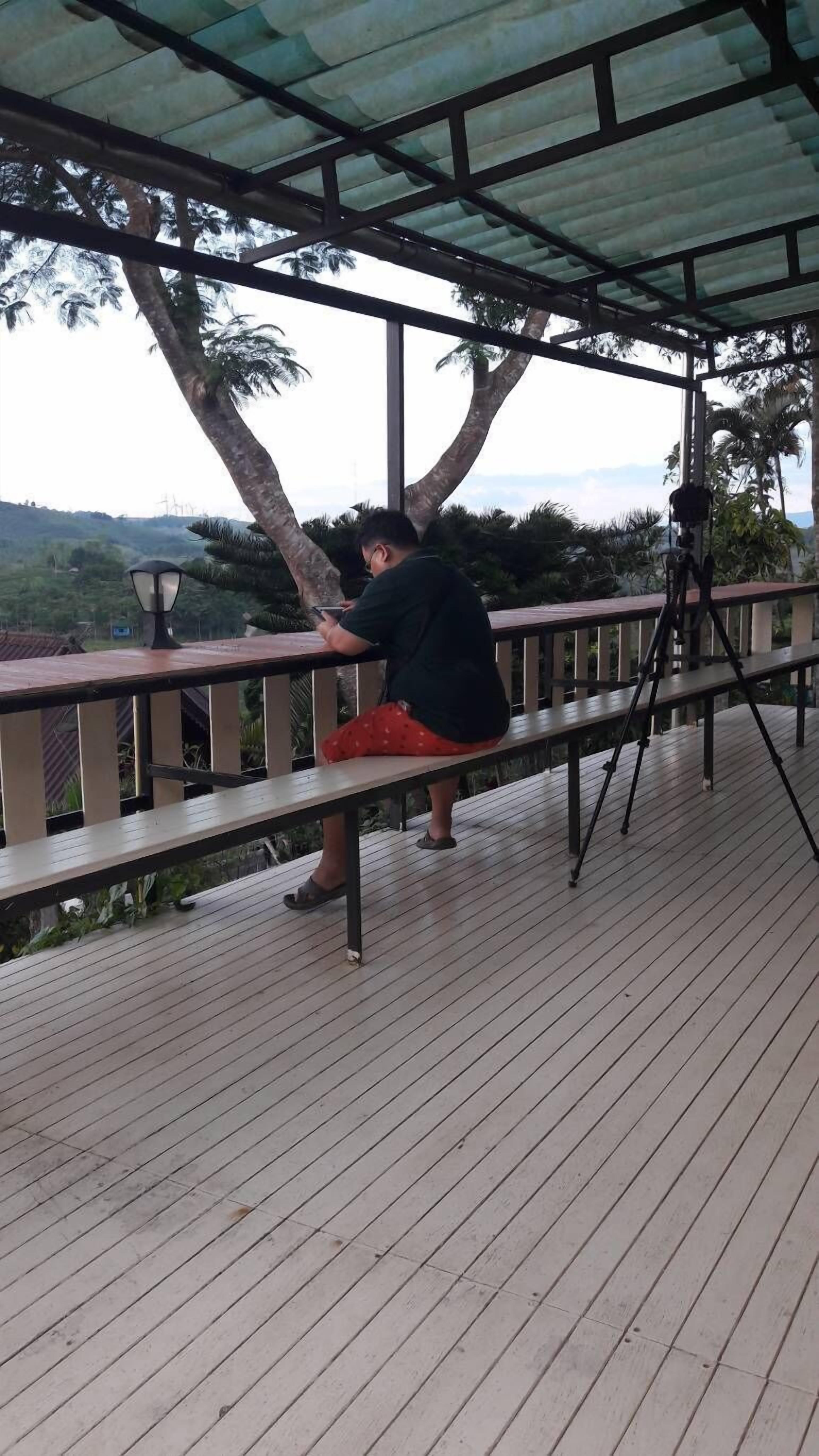 A covered outdoor area with a wooden deck, metal railing, and a person using a smartphone.