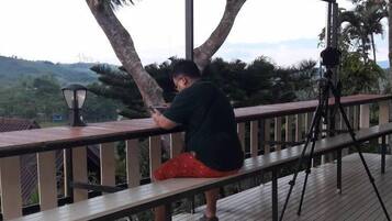 A covered outdoor area with a wooden deck, metal railing, and a person using a smartphone.