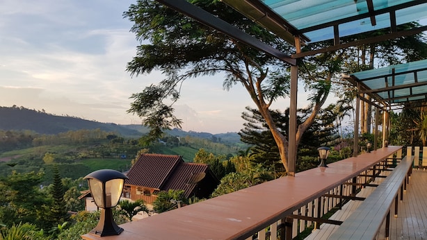 Una terraza de madera con una larga mesa y bancos, con vistas a un valle exuberante.