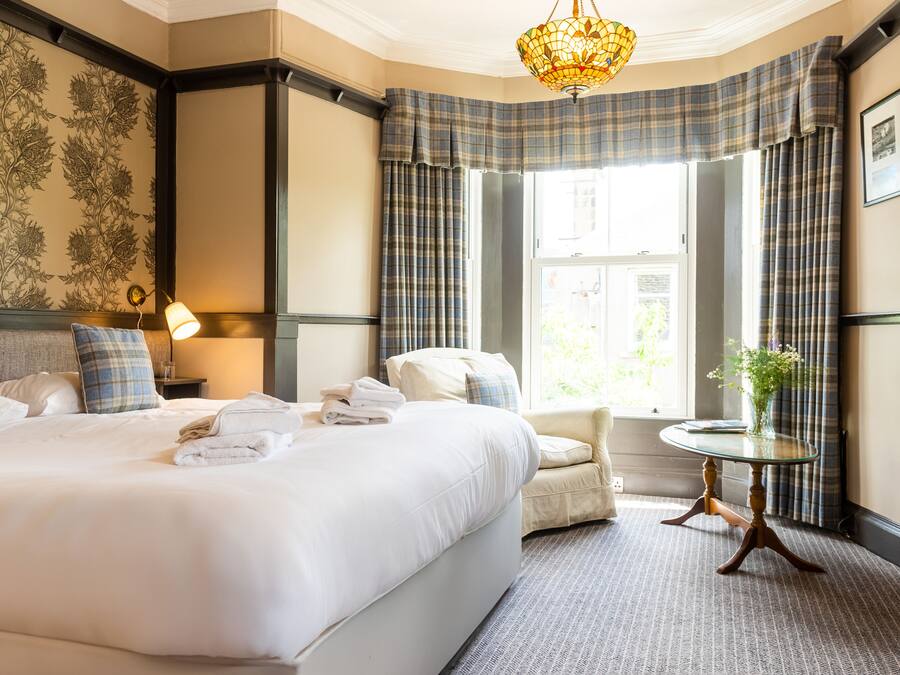 A hotel room with a large bed, a sitting area, a small table, and a window with curtains.