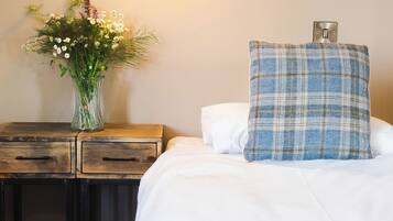 A hotel room with a bed, a nightstand with a vase of flowers, and a wall-mounted lamp.