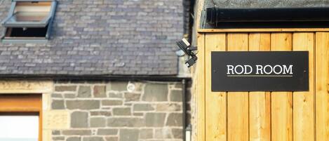 Una puerta de madera con la leyenda "ROD ROOM", un muro de piedra y una ventana al fondo.