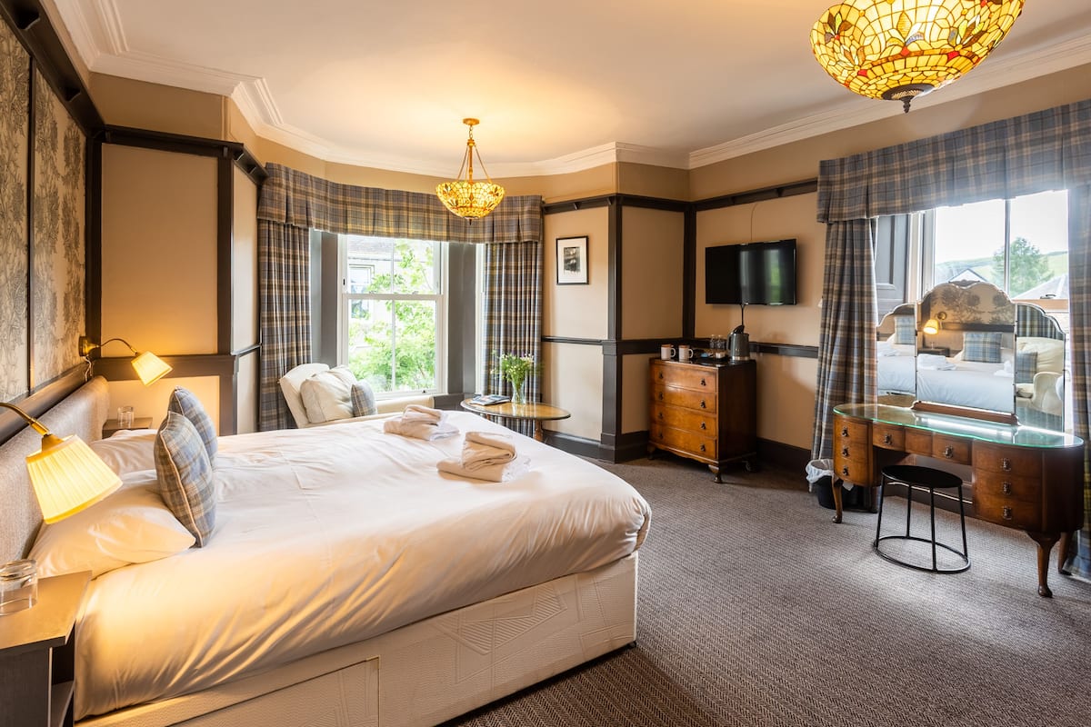 A hotel room with a large bed, a desk, a chair, a dresser, and a television.