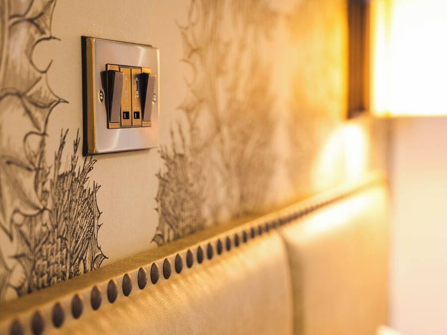 A hotel room with a bed, a wall-mounted light switch, and a decorative wall panel.