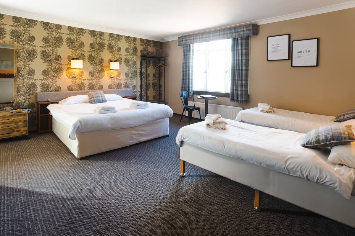 A hotel room with two beds, a small table, a chair, and a wardrobe.