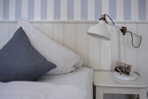 A neatly made bed with a white and gray pillow, a white bedside table with a lamp, and a small photo frame. - Kellers Badehotel (Fano)