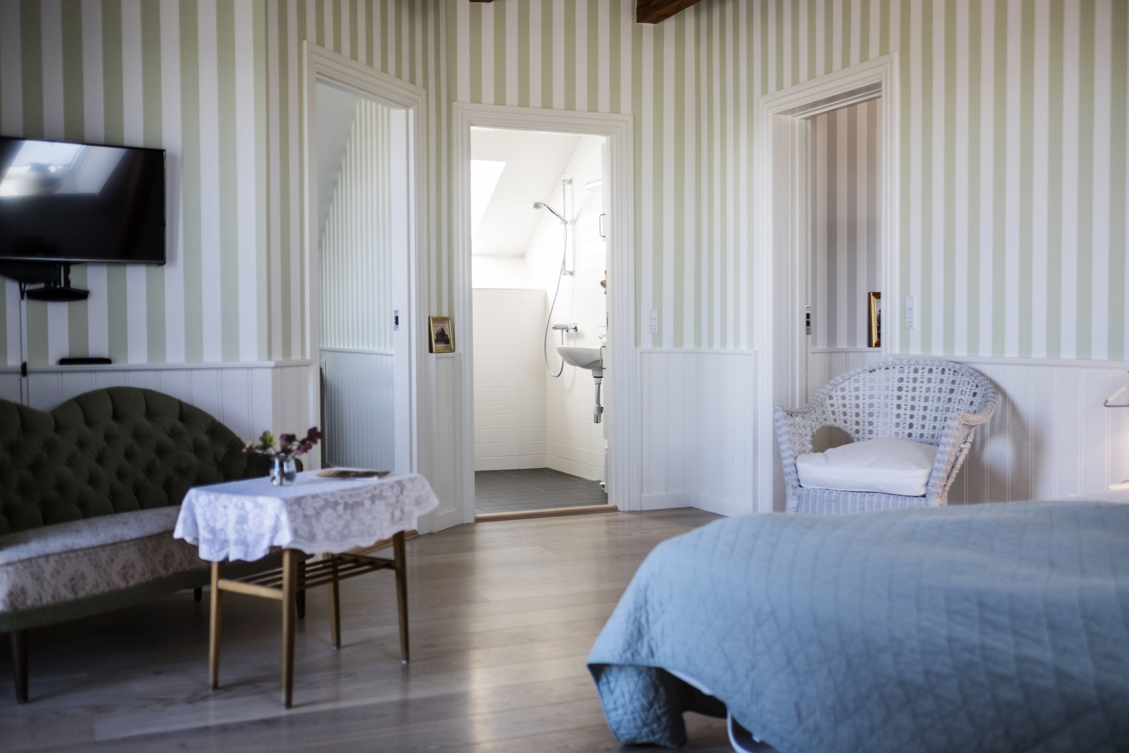 Et hotelværelse med sofa, et lille bord med en vase, et fjernsyn, en fletstol og en seng.