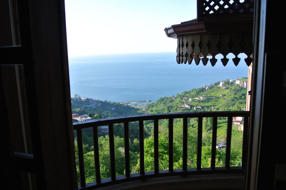 A balcony with a view of a coastal landscape, including a body of water and green hills.