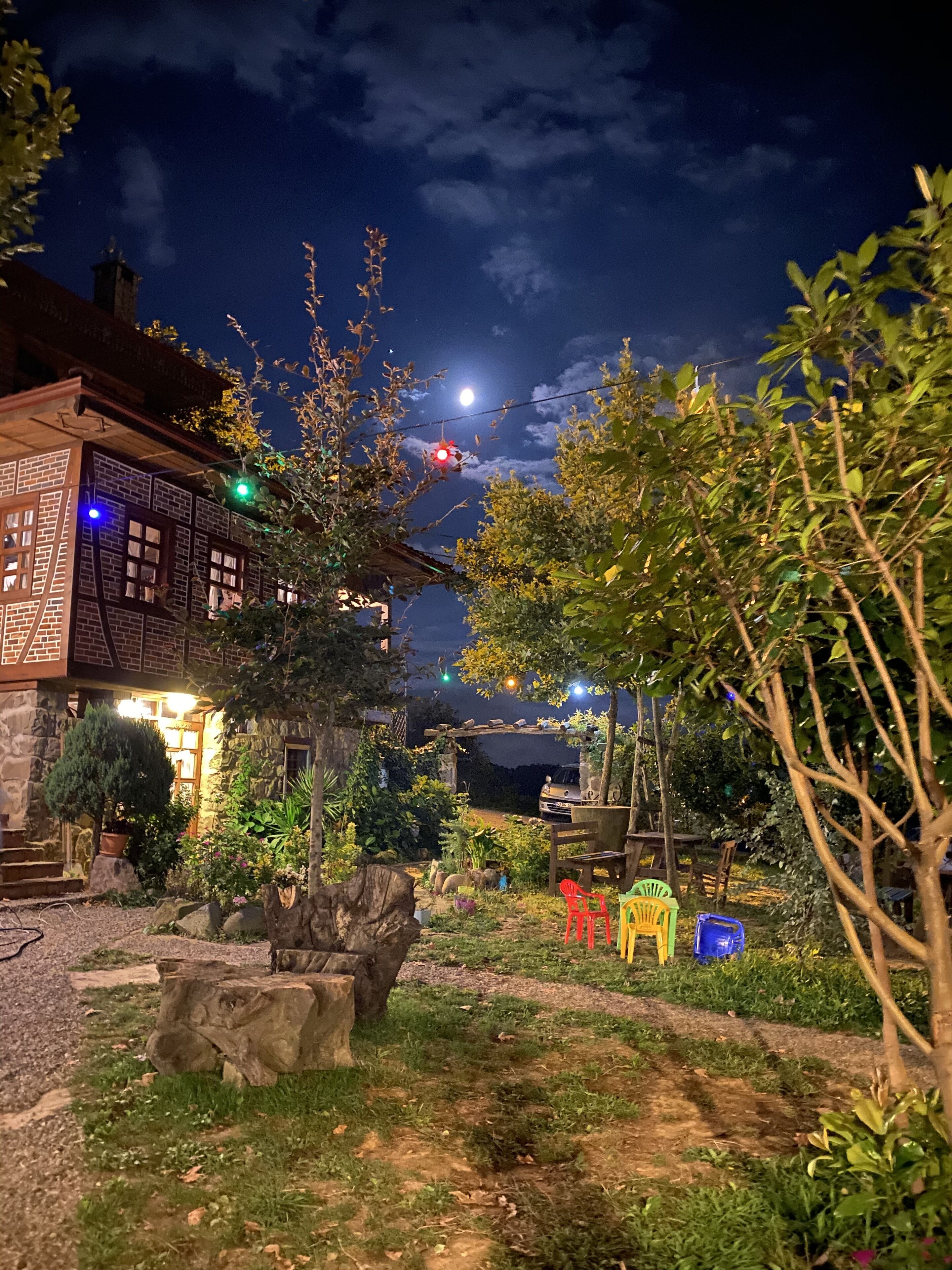 A rustic building with a stone facade, a wooden deck, and a garden with various plants and a small pond.