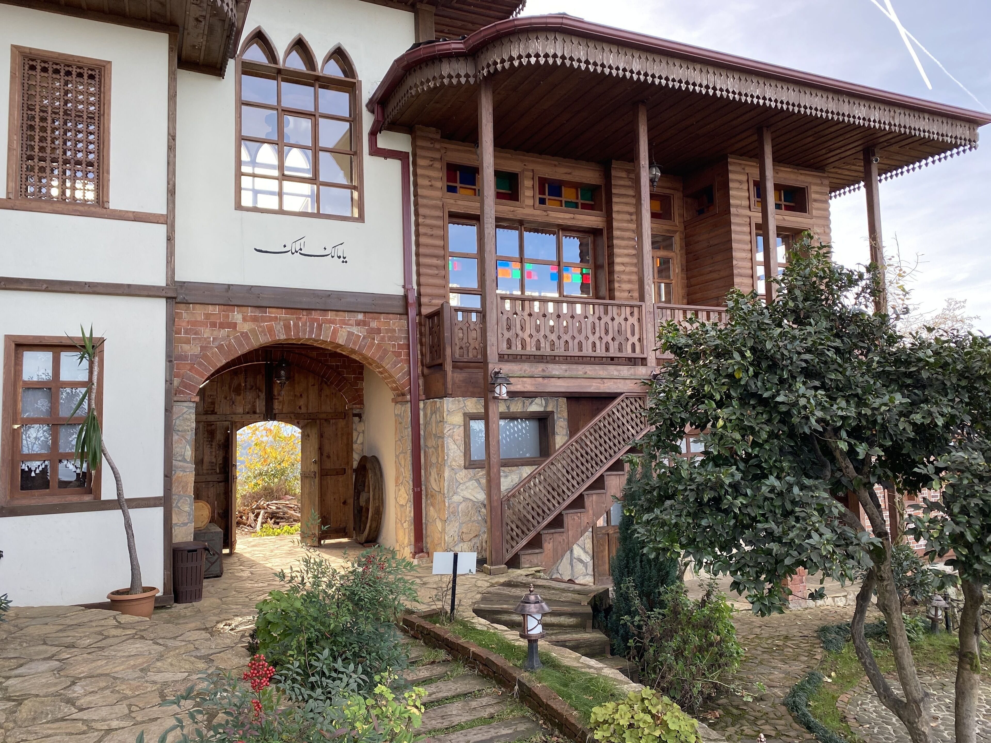 A traditional wooden building with a balcony, stone steps, and a small garden area.