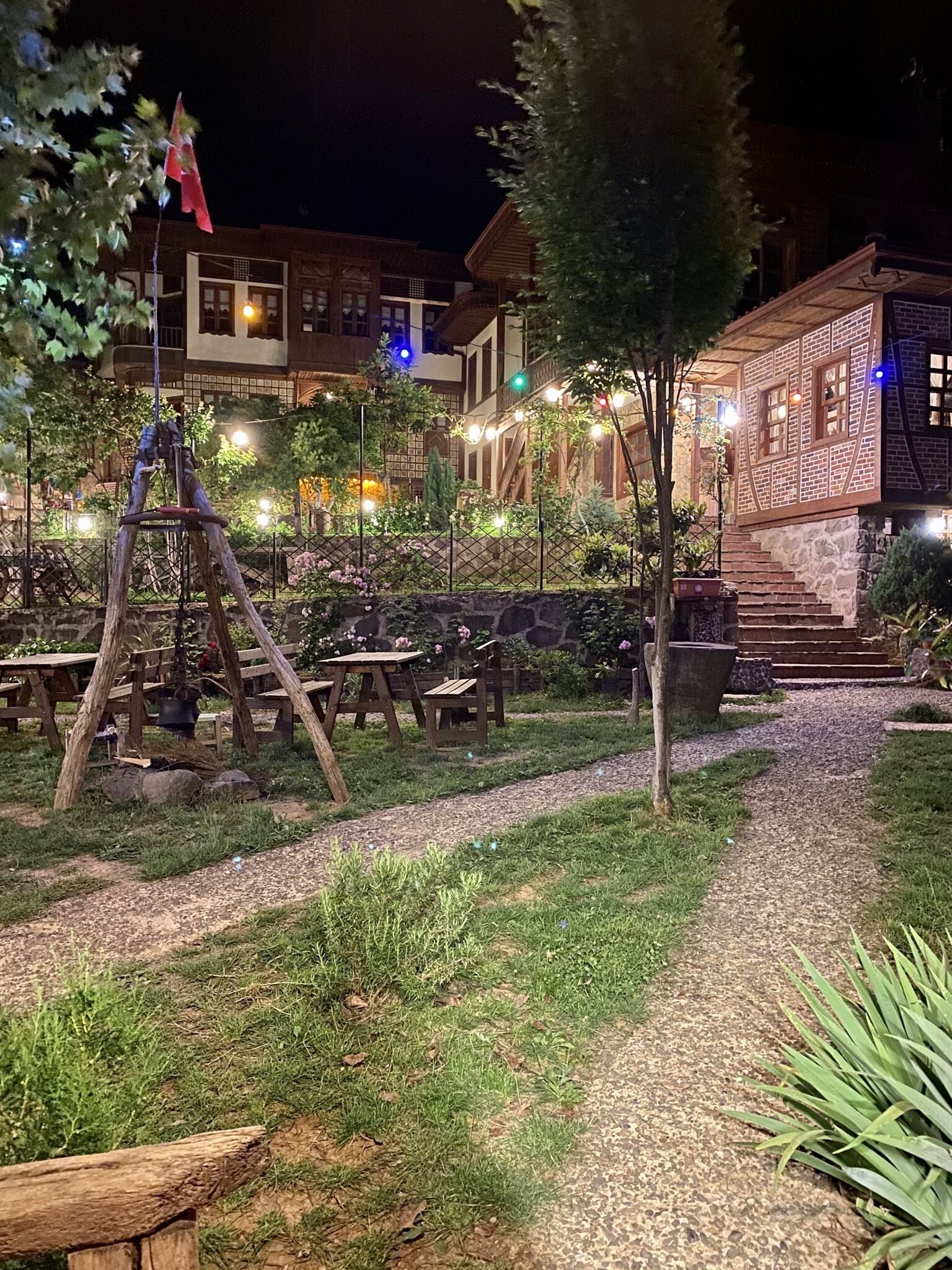 An outdoor area with picnic tables, a swing set, and a building with string lights.