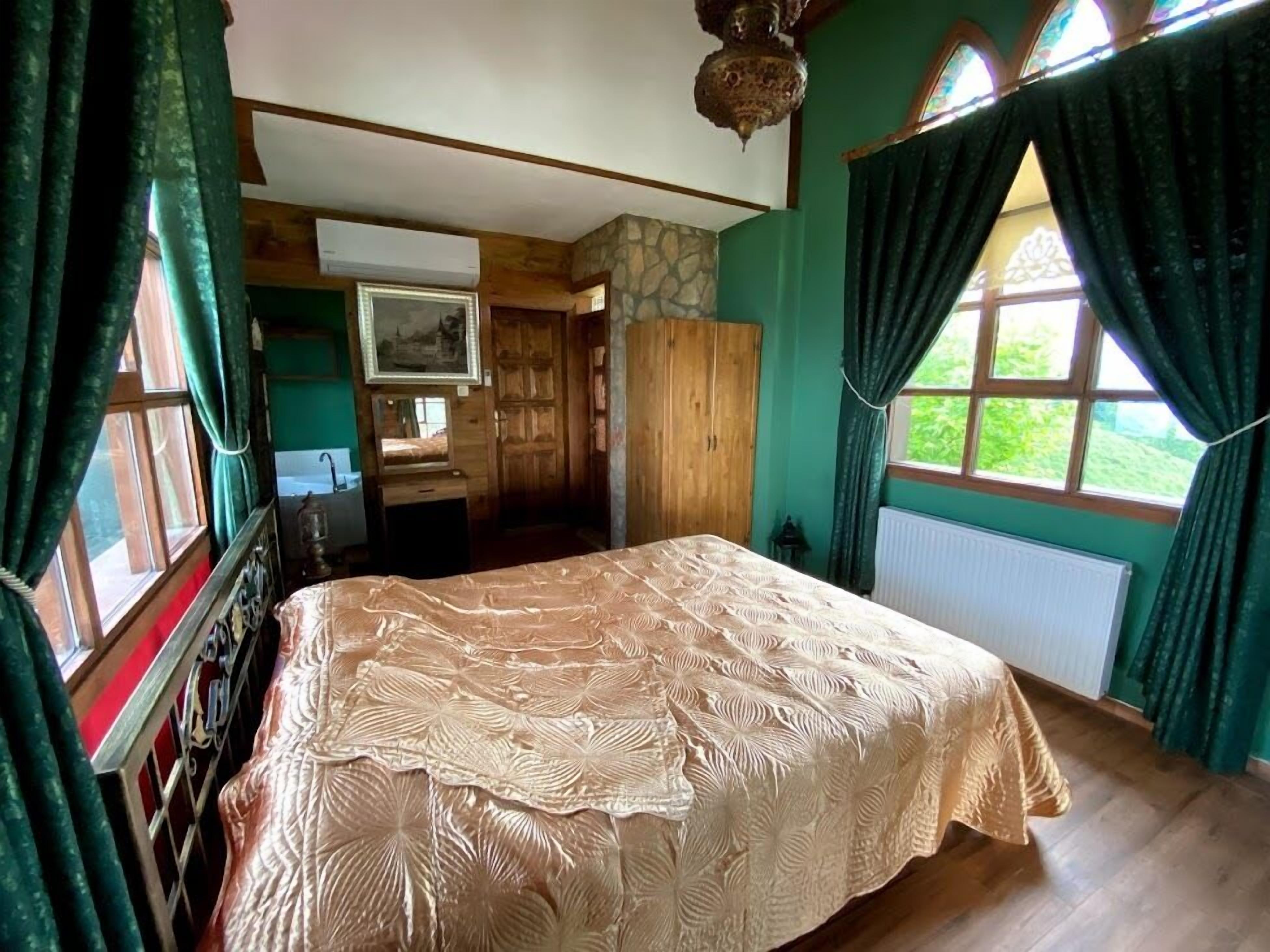 A bedroom with a large bed, a wooden wardrobe, a mirror, and a window with curtains.