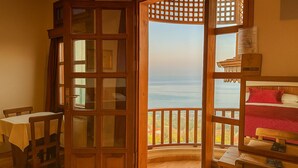 A room with a wooden door leading to a balcony with a view of the sea. There is a bed with red bedding and a small table with chairs. - Kafdagi Konak Hotel (Derepazari)