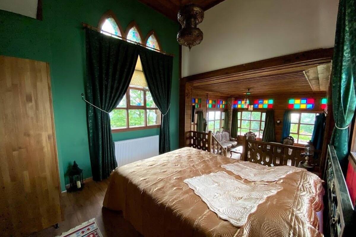 A room with a large bed, wooden furniture, and a view of greenery through the windows.