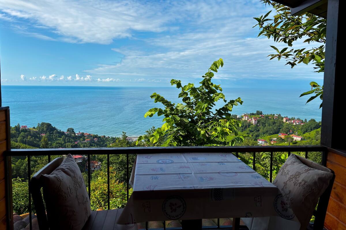 A balcony with a table and chairs, overlooking a coastal view with buildings and greenery.
