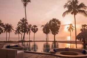 A poolside area with lounge chairs and a hot tub, overlooking the ocean at sunset.