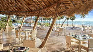 An outdoor dining area with thatched roof, wicker furniture, and a view of the beach and ocean. - Jetwing Surf & Safari, A Luxury Reserve (Pottuvil)