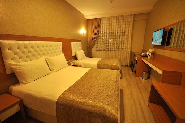 A hotel room with two beds, a wooden headboard, a TV, and a desk.