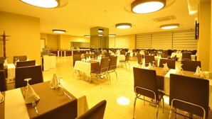 A large dining area with multiple tables and chairs, a kitchen in the background, and a bright, yellow-lit ambiance. - Bupa Hotel (Kayseri)