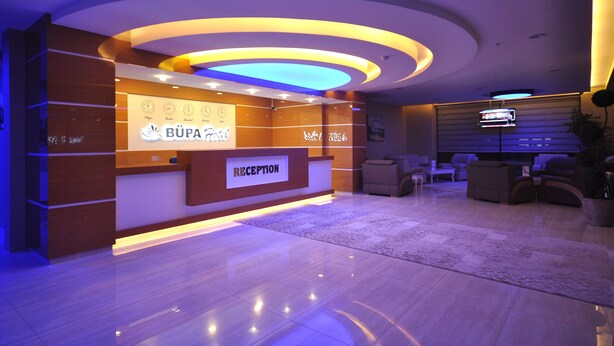 A reception area with a modern design, featuring a reception desk labeled "RECEPTION" and a digital clock displaying the time. - Bupa Hotel (Kayseri)